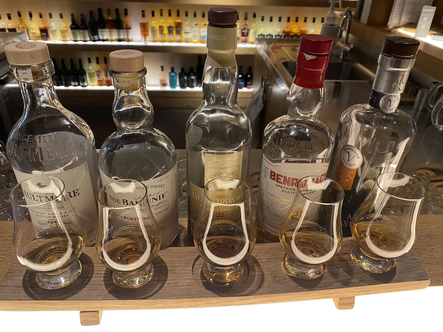A flight of five Scotch whiskies in nosing glasses, each set in front of its bottle