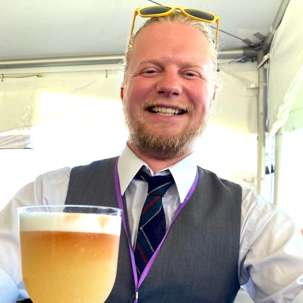 Jimmy Dickson in a vest and tartan tie, raising a pint